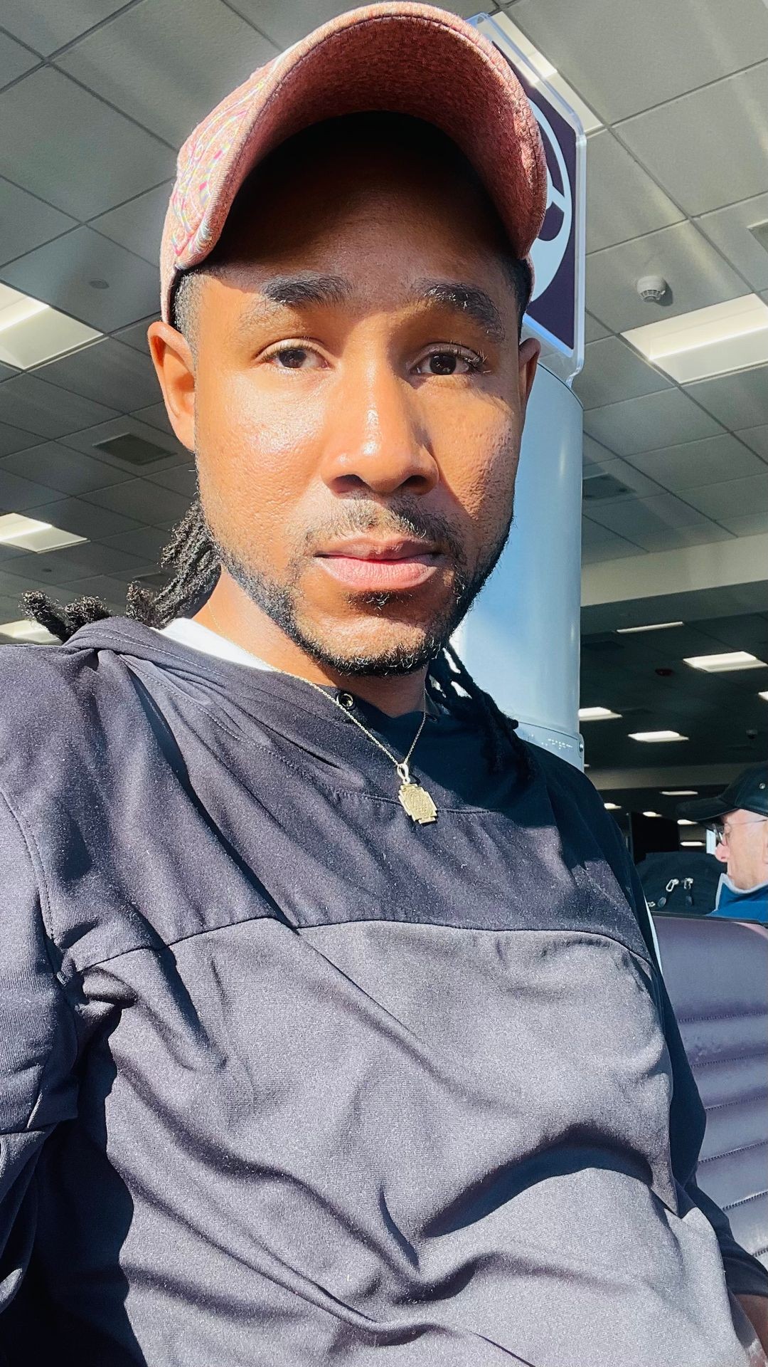 Person wearing a pink cap and black sweatshirt sitting indoors with sunlight on their face.