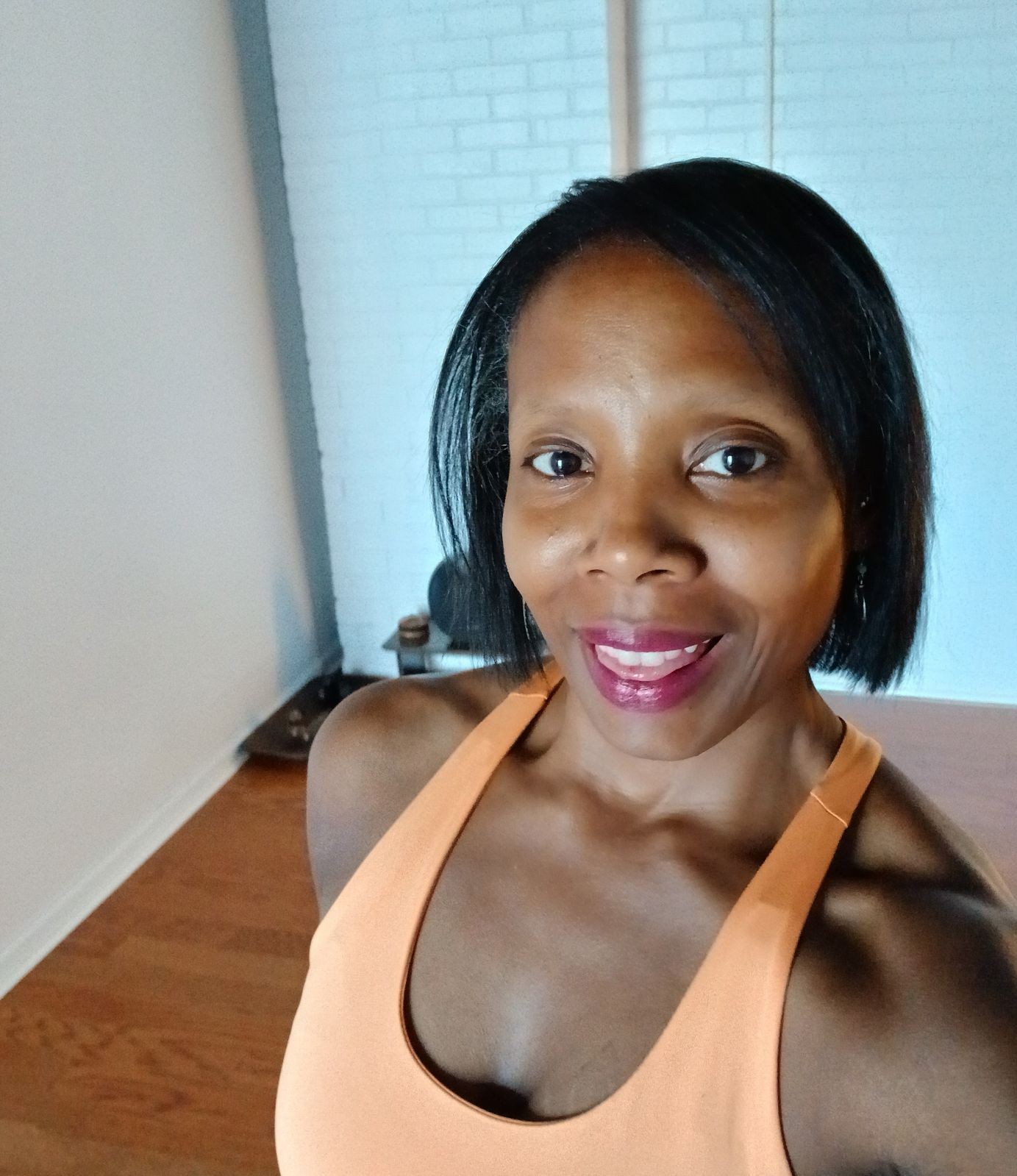 Person wearing an orange tank top standing in a room with wooden flooring and a white brick wall.