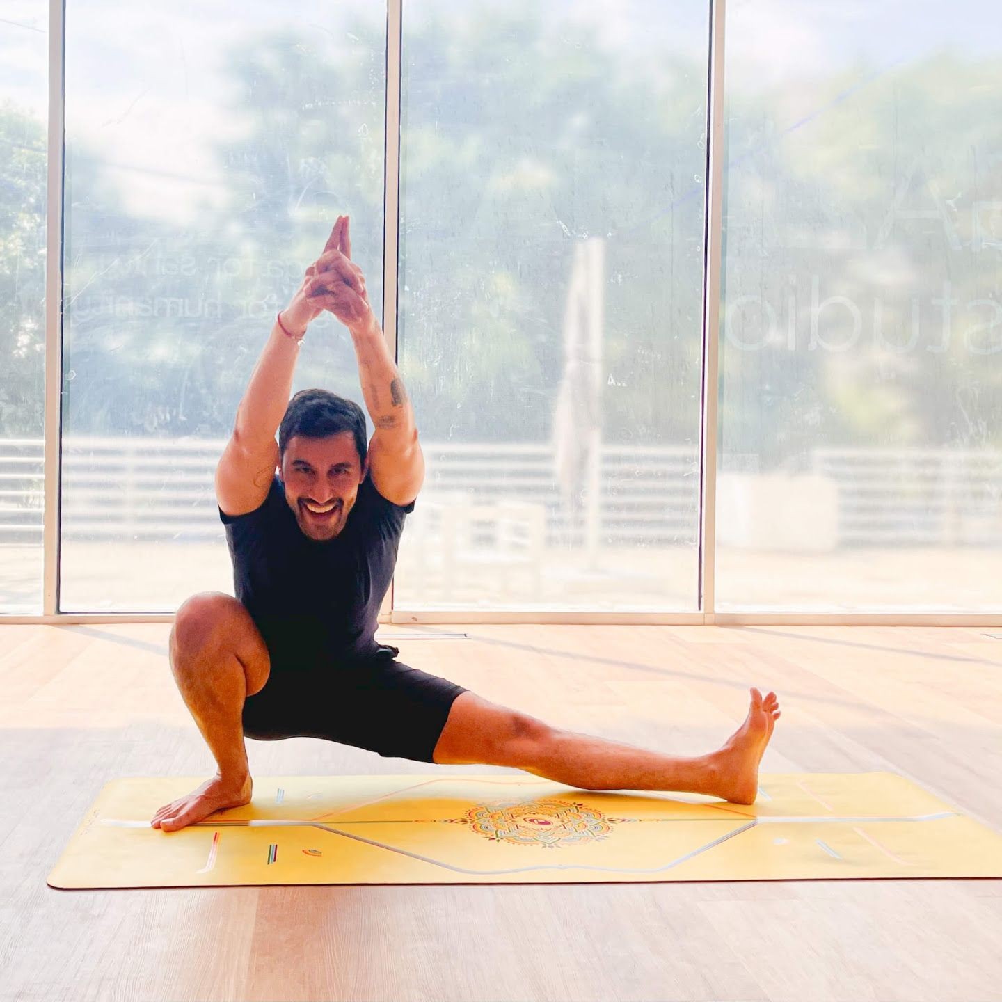 Person practicing yoga on a yellow mat in a well-lit room with large windows.